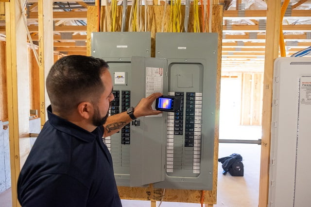 An inspector using a thermal camera to investigate newly installed electrical box during new construction pre drywall inspection.
